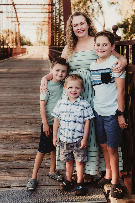 Sioux Falls family photography of a mother with her three sons standing on a historic bridge, wearing navy, white, and mint green outfits while smiling at the camera