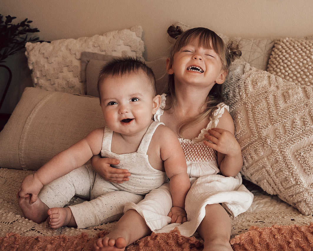 baby and toddler sibling milestone portrait sitting on neutral bed during lifestyle children photography session near Sioux Falls South Dakota