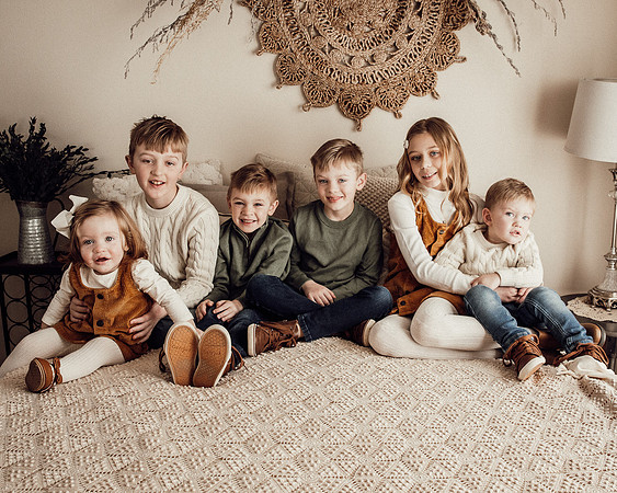family of six kids sitting together on a cream colored neutral bed during a warm indoor lifestyle family Sioux Falls photography session