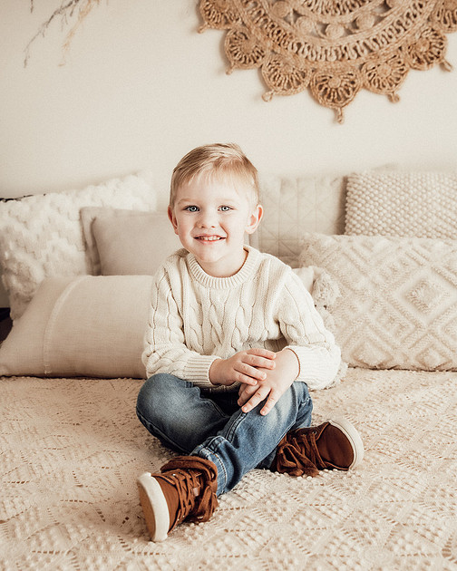 3 year old boy sitting on a cream colored neutral bed during a milestone portrait session celebrating his third birthday