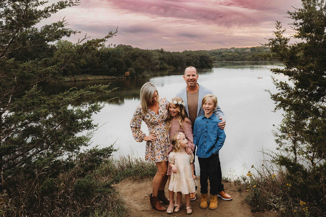 Sioux Falls Photographer captures Family of five smiling together in front of a peaceful lake.