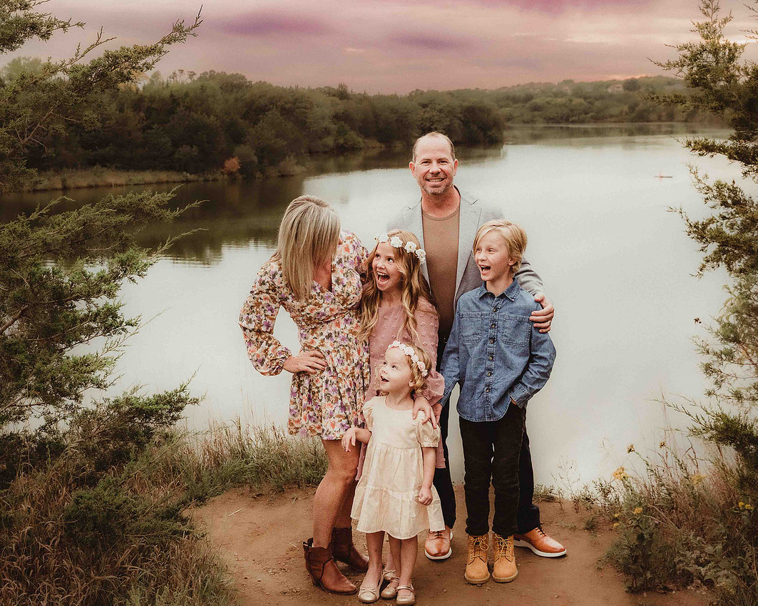 Family of five wearing coordinated pastel outfits during a spring sunset session with violet and magenta sky, featuring textures, patterns, floral crown, and layered styling
