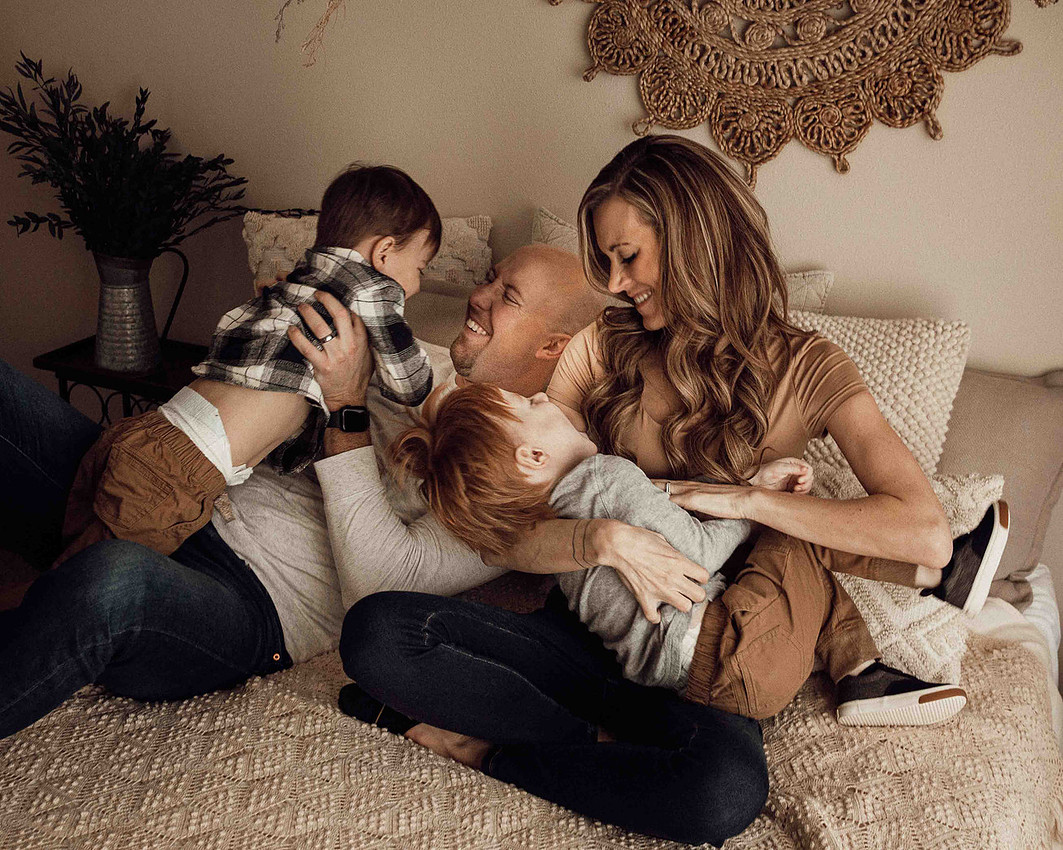 Sioux Falls family of four with twin toddler boys sitting on a neutral cream bed, parents tickling each child while everyone laughs and smiles in a joyful lifestyle photography session