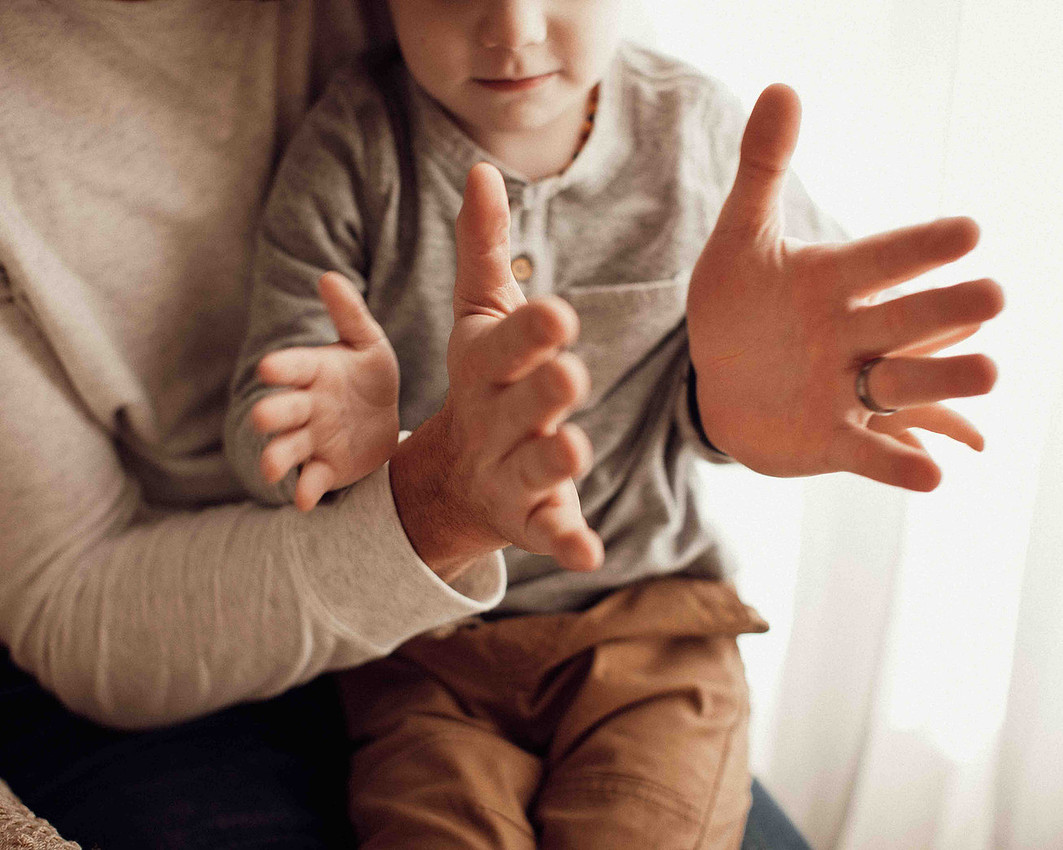 Close-up of father and young son playing a clapping game on a bed during a Sioux Falls family photography session, focusing on their hands and interaction from nose to knees