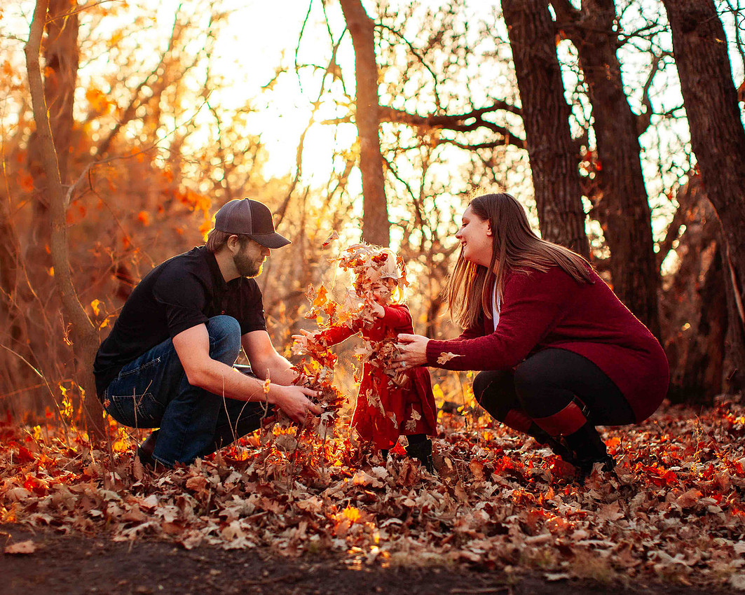 Family playing in leaves at sunset with young child during candid lifestyle photography session