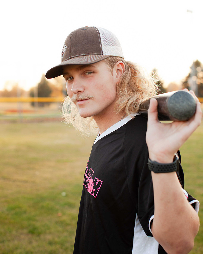 Sioux Falls senior photographer capturing confident high school senior baseball player holding bat with smug smile during outdoor portrait session