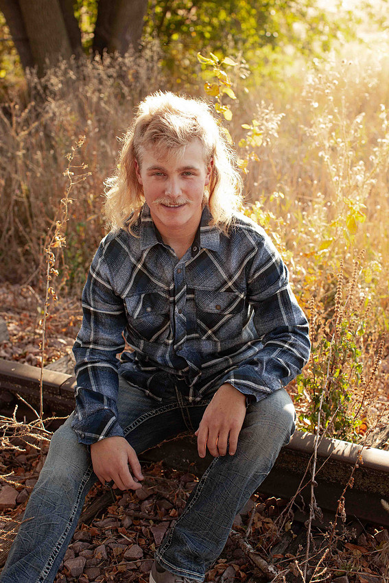 Sioux Falls senior photographer capturing high school senior guy sitting on railroad tracks wearing flannel shirt and jeans outdoor portrait