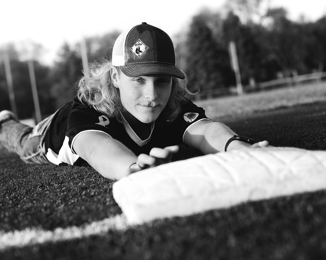 High school senior baseball player diving headfirst into base on the infield, wearing a uniform with jeans and a baseball cap, showing effort and determination