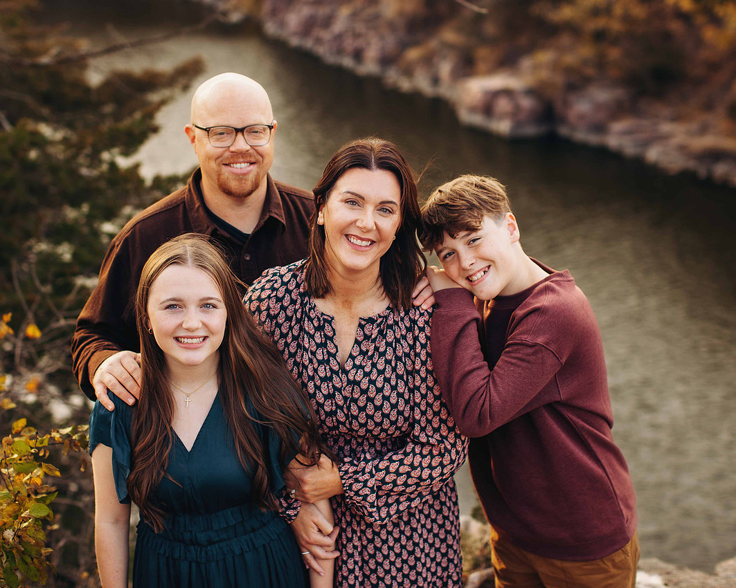 Family of four with older children wearing coordinated fall outfits in navy, teal, burgundy, and tan, styled with textures and patterns for a cohesive outdoor portrait