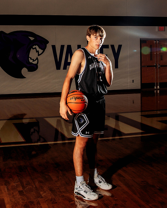 High school senior basketball player holding a basketball and adjusting his jersey collar with dramatic sideline rim lighting, creating a strong and focused athletic portrait