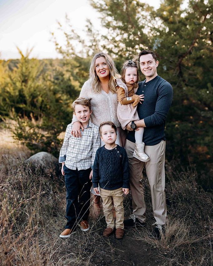 Family of five wearing coordinated outfits with mixed textures and patterns including knits, woven fabrics, and soft layers, creating a warm and cohesive family portrait