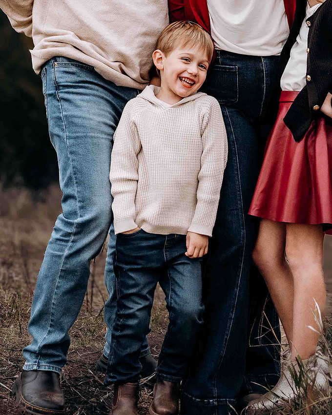 Young boy smiling in cozy sweater and jeans during outdoor family photo session