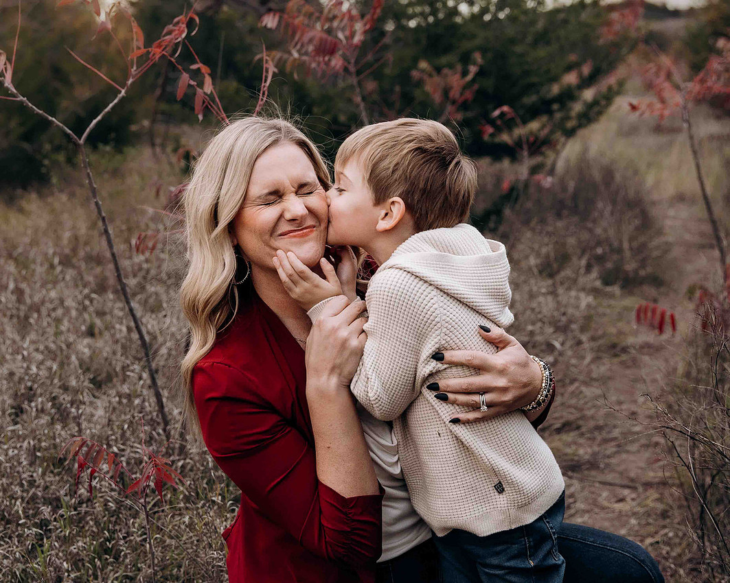 Young boy kissing his mother on the cheek during a heartfelt outdoor family photography moment
