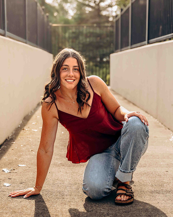 high school senior girl posing in red tank top and jeans during outdoor senior portrait session. Sioux Falls South Dakota