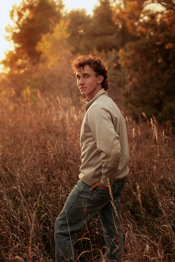 Senior boy wearing jeans and a white quarter-zip sweatshirt standing in a golden fall field at sunset during a Sioux Falls South Dakota senior photography session.