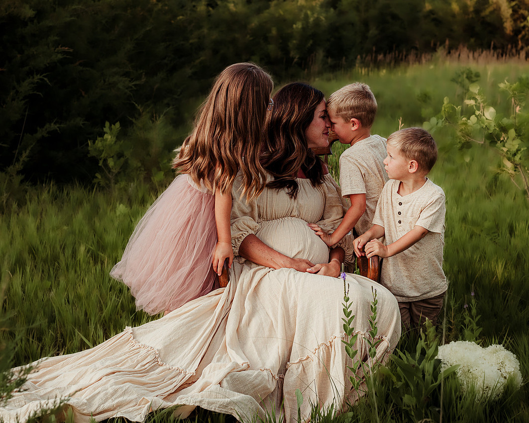 Mother with children in grassy field during maternity family photography session near Sioux Falls South Dakota.