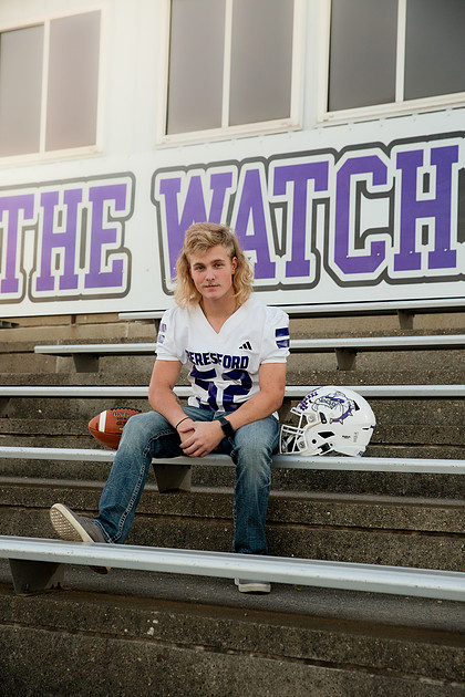 Beresford High School senior football player sitting on stadium bleachers with football helmet beside him during a senior portrait session.
